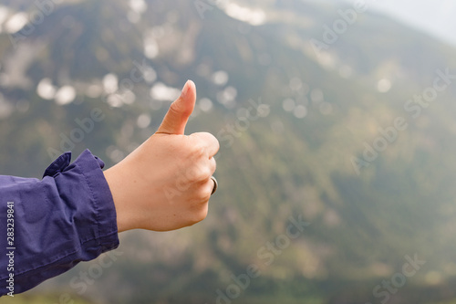 Happy fimale traveler showing thumb up in spring mountains, point of view shot