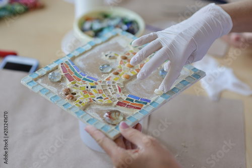 Process of making a mosaic picture from ceramic tile. The man organizes with a tweezers a puzzle of ceramic elements to build a picture.