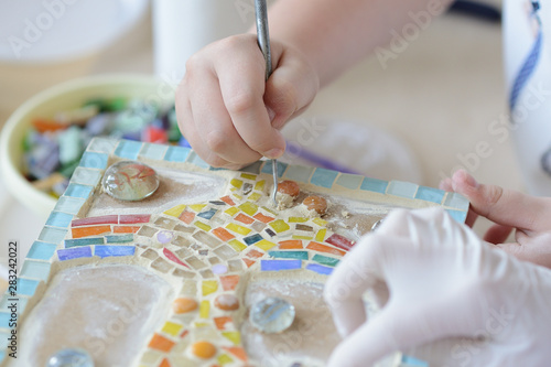 Process of making a mosaic picture from ceramic tile. The man organizes with a tweezers a puzzle of ceramic elements to build a picture.