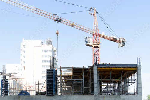 A construction crane works in the morning at the facility. Boom crane on the construction of a high-rise building. Blue sky, high-rise building.