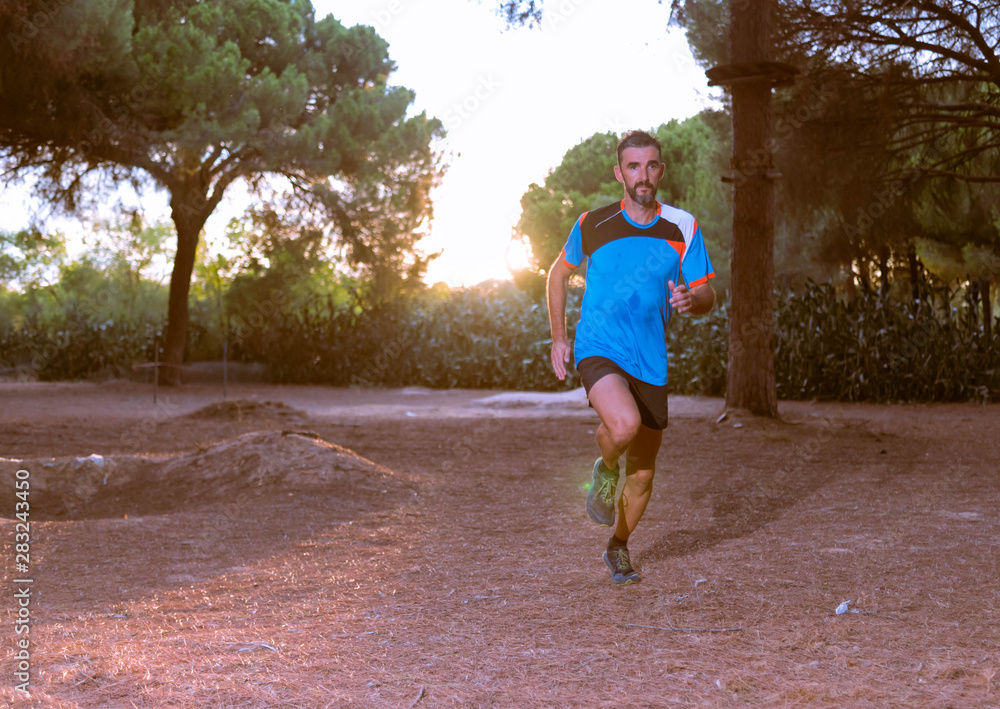 Middle aged caucasian man trail running in forest at sunset