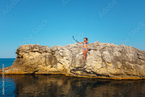 A girl in a blue swimsuit with a camera jumps into the sea from a cliff