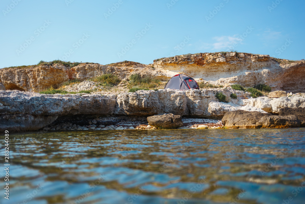Gray tent on a rocky seashore. View from the water