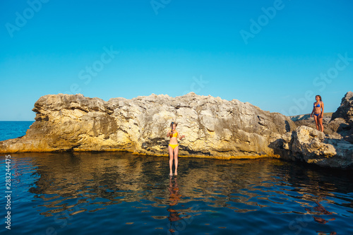 A girl in a yellow swimsuit with a camera jumps into the sea from a cliff