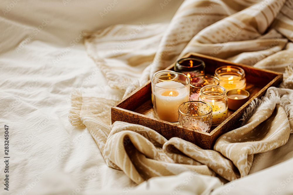 Obraz na płótnie Burning candles on wooden tray with warm plaid in bed.  Scandinavian style. Hygge concept. w salonie