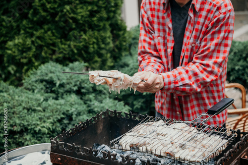 Man holds skewer with meat over barbecue