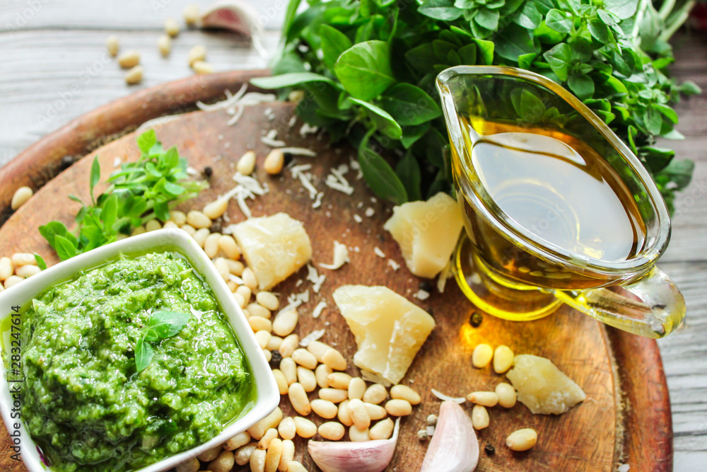 Close-up of a bowl with pesto sauce and ingredients for its preparation: green Basil, Parmesan cheese, olive oil, pine nuts, salt and garlic on the background of aged boards