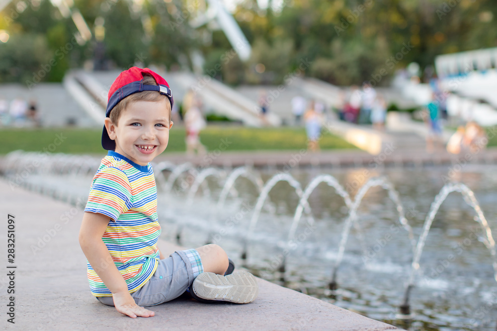 Naklejka premium baby Boy sitting near the fountain in the city park