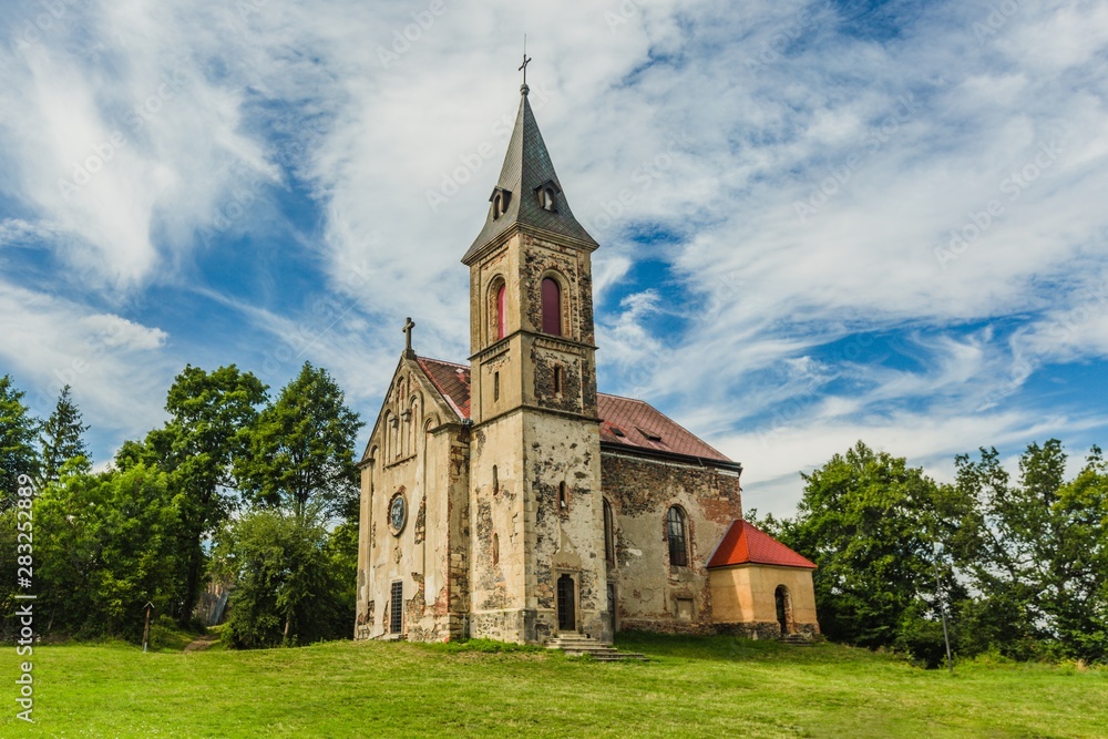 Krasikov, Kokasice / Czech Republic - August 9 2019: View of the old church of Mary Magdalene. Bright sunny summer day with blue sky and white clouds, green grass and trees.