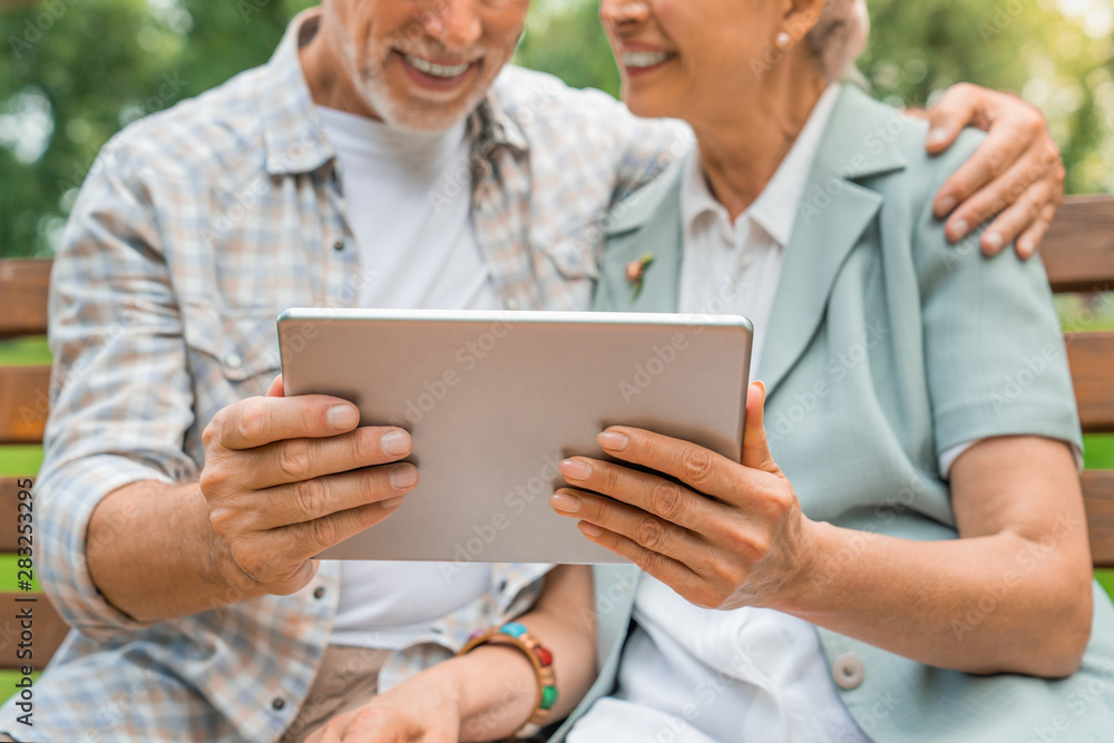 Cropped shot of old man and woman using tablet pc at park bench. Focus on tablet