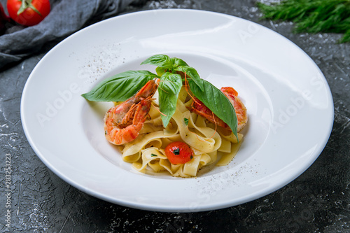 Pasta fettuccine with shrimps, tomatoes and basil on grey concrete background