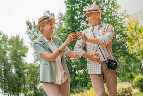 Low angle view happy elderly man and woman walking in park drinking coffee and having fun © InsideCreativeHouse