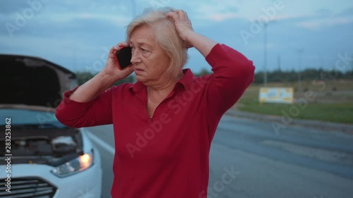 Sad senior businesswoman speak on phone stand near opening the hood broken down car driver road service emergency travel woman auto breakdown call down nature slow motion photo