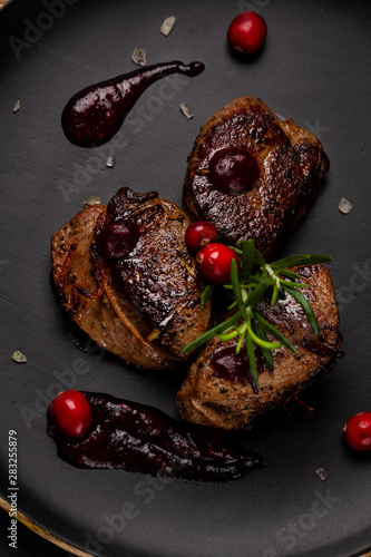 Venison or deer steak with ingredients like sea salt, rosemary and cranberry on black plate. Food background for restaurant. Top view photo