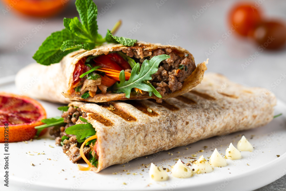 Tortilla wraps sandwiches with fresh vegetables, minced meat and blood oranges on plate. Burrito, sandwich wrap, fajita wrap Tortilla wraps sandwiches with fresh vegetables, minced meat and blood oranges on plate. Burrito, sandwich wrap, fajita wrap