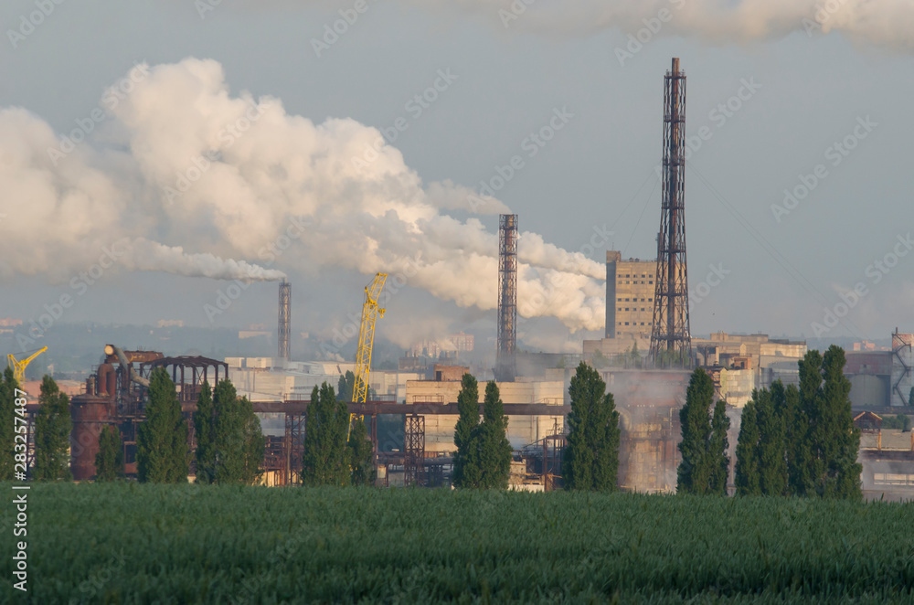 smoke from the chimney of a working plant on a background of green wheat field, concept of respect for nature.