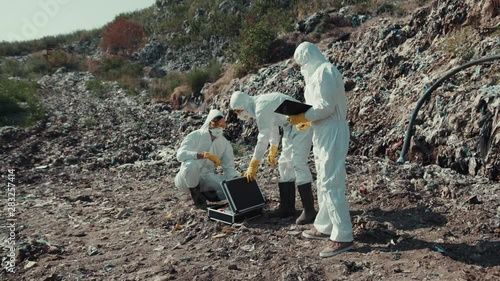 Ecological disaster. View of men scientists in chemical protection collecting samples of rubbish on pulluted land in disposal site. photo