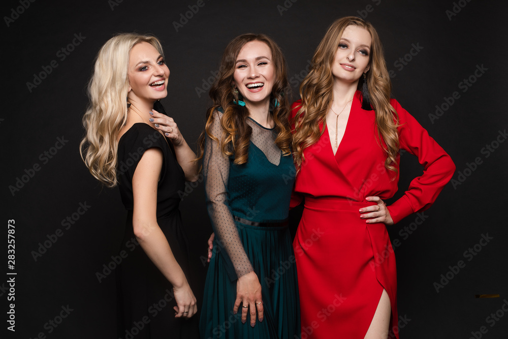 Studio full length portrait of three stunning young ladies in evening gowns posing for camera. Black background. New Year evening celebration birthday concept. Studio full length portrait of three stunning young ladies in evening gowns posing for camera. Black background. New Year evening celebration birthday concept.