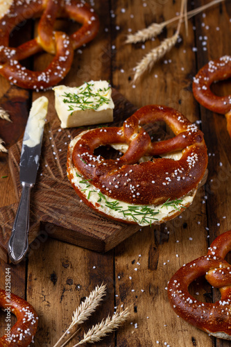 Freshly baked homemade soft Brezel with salt, butter and chive on rustic wooden table. German pretzel called Brezel.