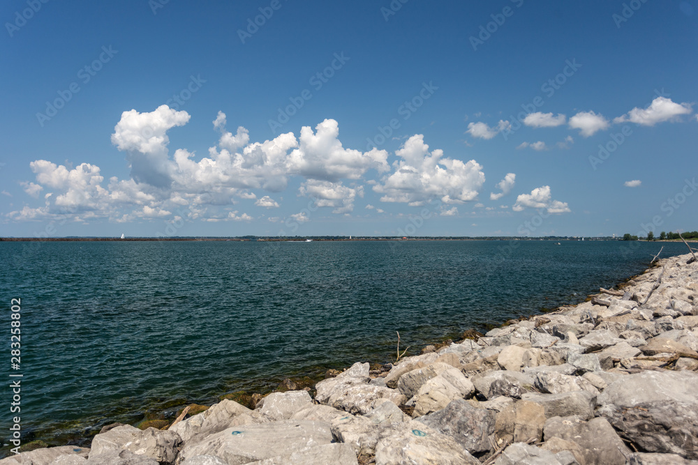 Clear blue lake with grey rocks in the foreground and beautiful clouds in the sky Clear blue lake with grey rocks in the foreground and beautiful clouds in the sky