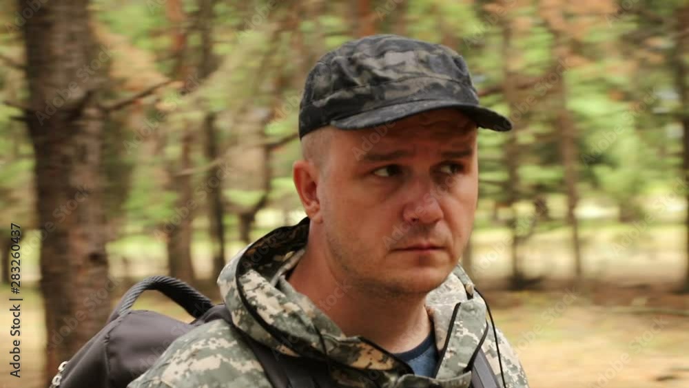 The camera moves around a caucasian handsome traveler in camouflage clothing, a cap and a backpack sitting on a log in a dense green forest, medium plan The camera moves around a caucasian handsome traveler in camouflage clothing, a cap and a backpack sitting on a log in a dense green forest, medium plan