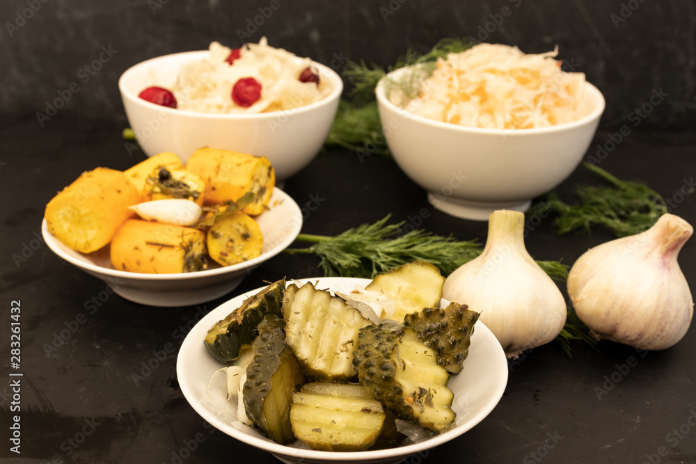Fermented vegetables in two white bowls and two white plates on a dark background.