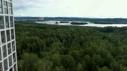 flying near high-rise modern house over the forest and past the building, river view on the horizon. Modern residential area in a green area. photo