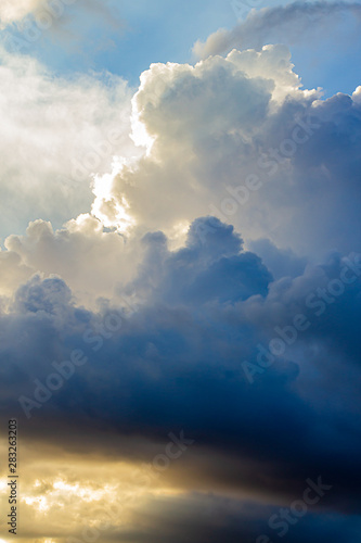 large cumulus, nimbus clouds with silver lining, in blue, gold and white © Taya