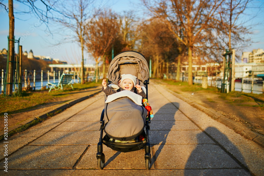 Obraz premium Adorable happy little girl sitting in pushchair outdoors