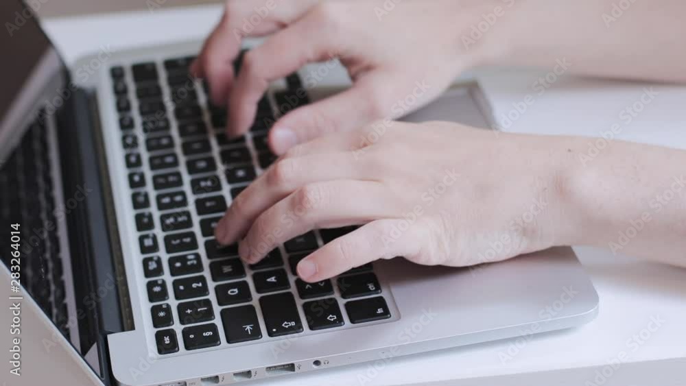Hands typing quickly on a laptop keyboard in a clear home office space Hands typing quickly on a laptop keyboard in a clear home office space