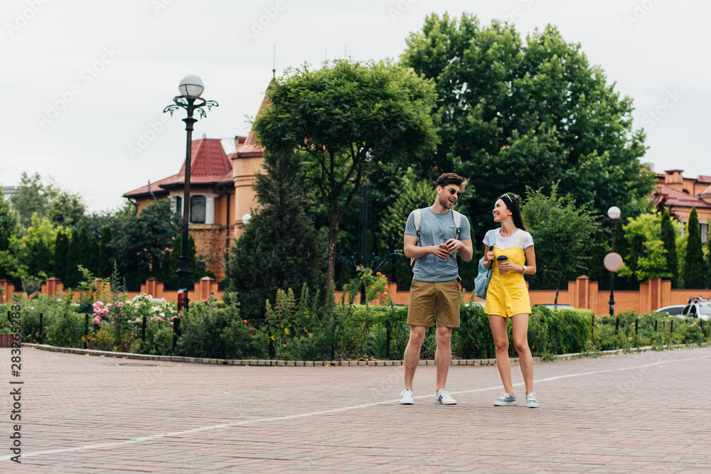 Obraz premium handsome man and asian woman smiling and holding paper cups