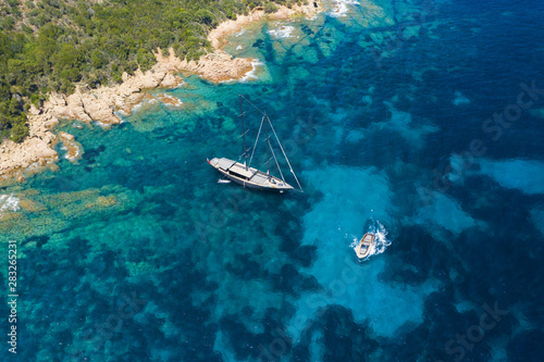 View from above, stunning aerial view of a luxury sailboat floating on a beautiful turquoise clear sea that bathes the green and rocky coasts of Sardinia. Emerald Coast (Costa Smeralda) Italy.