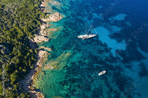 View from above, stunning aerial view of a luxury sailboat floating on a beautiful turquoise clear sea that bathes the green and rocky coasts of Sardinia. Emerald Coast (Costa Smeralda) Italy.