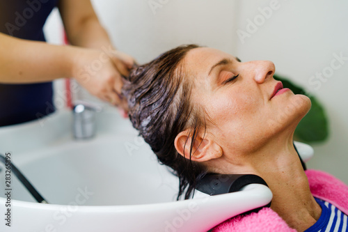 Hairdresser washing hair of woman female customer with a shower at the saloon applying shampoo on wet hair