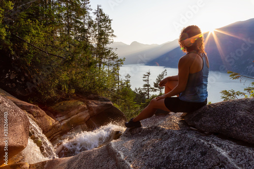 Adventurous Girl is sitting on top of a Beautiful Waterfall, Shannon Falls, and watching the sunset. Taken near Squamish, North of Vancouver, British Columbia, Canada.
