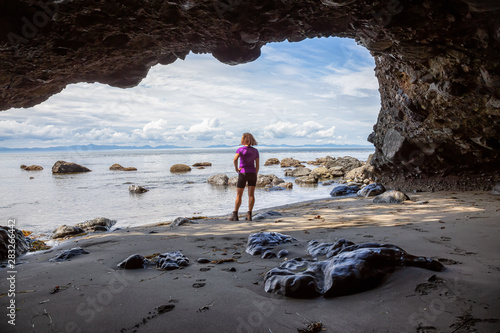 Adventurous girl hiking in a cave on Juan de Fuca Trail to Mystic Beach on the Pacific Ocean Coast during a sunny summer day. Taken near Port Renfrew, Vancouver Island, BC, Canada. photo