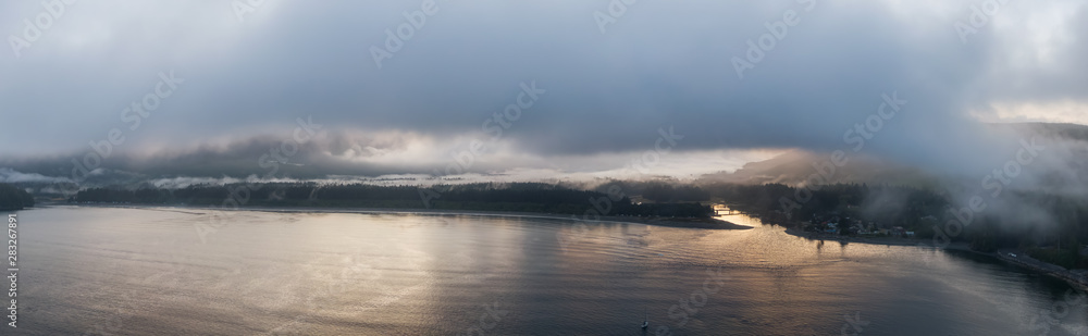 Aerial Panoramic View of a small secluded town on the Pacific Ocean Coast during a cloudy summer sunrise. Taken in Port Renfrew, Vancouver Island, BC, Canada.