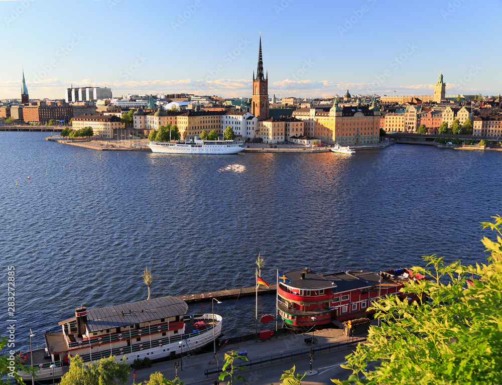 Obraz premium Scenic view of Stockholm's skyline including Gamla Stan illuminated at dusk with colorful boats on the foreground, Sweden