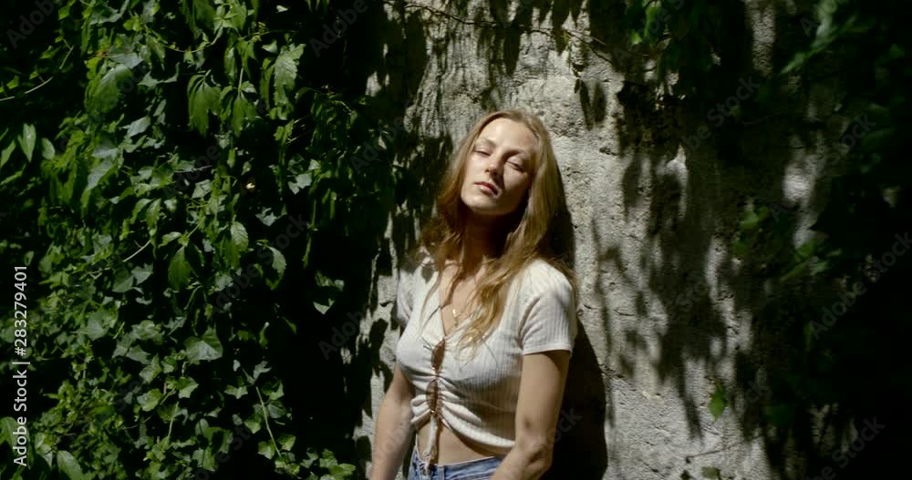 Portrait of a young blonde girl model who leaned against a tree among the green leaves, her top and denim shorts, touching her hair, posing. Portrait of a young blonde girl model who leaned against a tree among the green leaves, her top and denim shorts, touching her hair, posing.