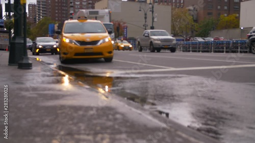 Iconic New York taxi Cab Drives Into Puddle On NYC Street While Pedestrians Walk By And Classic New York Traffic Commutes In Beautiful New York City
