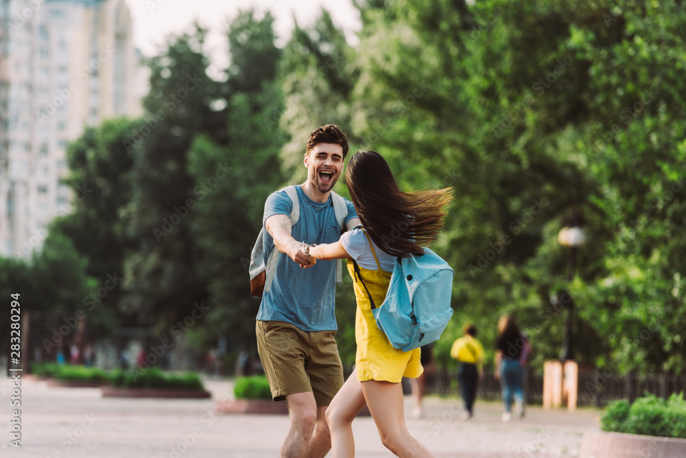 handsome man and woman with backpacks smiling and holding hands