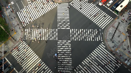 4K High Angle aerial view wide shot of pedestrian man and woman tourist walking crossing the street crosswalk with traffic driving cars stopping on the road in summer at Ginza, Tokyo, Japan photo