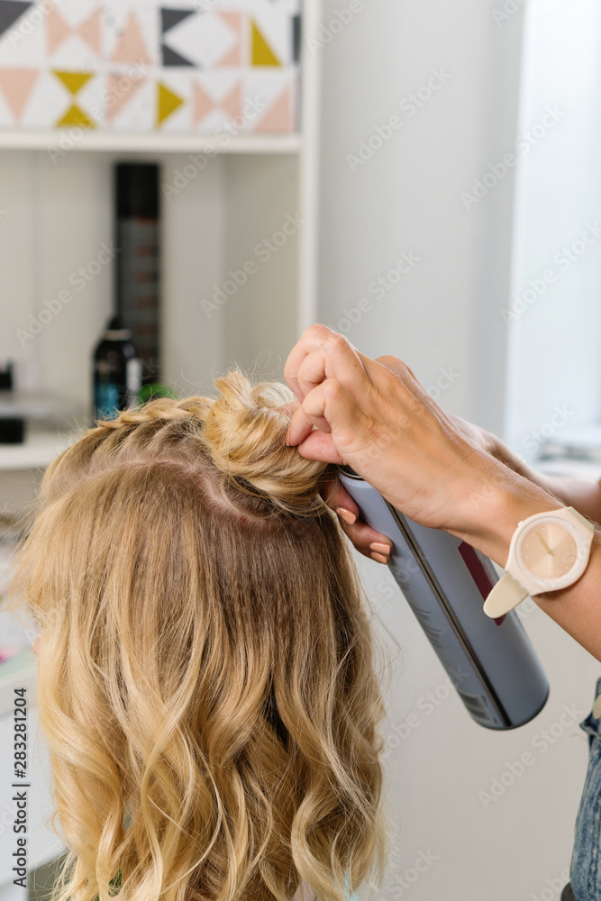 Fototapeta premium Hairtician builds upper bun. Hairstyle on bob. Hairdressing services. Creating evening hairstyles fashionable stylish women's hairstyles. Process of hair styling. Courses in hairdressing. Beauty salon