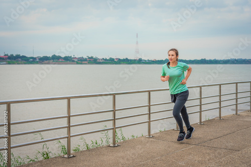 Fototapeta Naklejka Na Ścianę i Meble -  Woman running on the street with a view of the river in the morning.