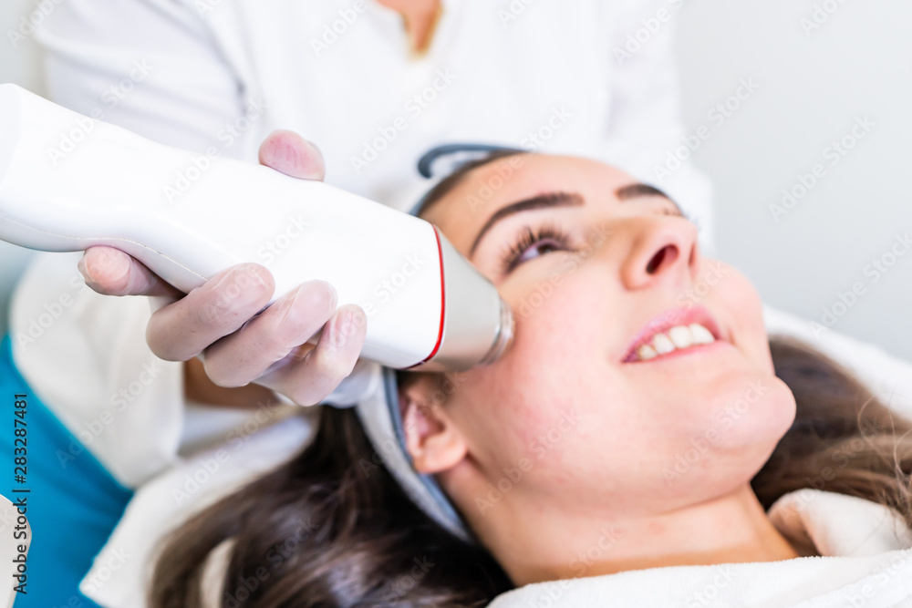 Radio frequency microneedling machine handpiece on the cheek of a woman's face during a beauty skin tightening treatment. Radio frequency microneedling machine handpiece on the cheek of a woman's face during a beauty skin tightening treatment.