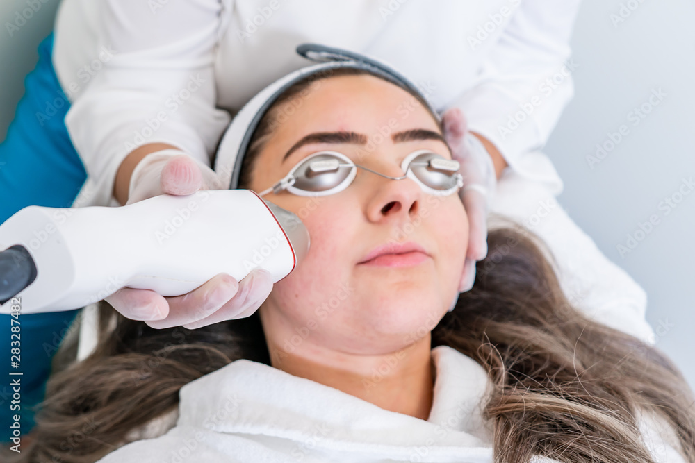 Beautician applying radio frequency microneedling handpiece to a woman's face for skin tightening treatments at a beauty clinic. Beautician applying radio frequency microneedling handpiece to a woman's face for skin tightening treatments at a beauty clinic.