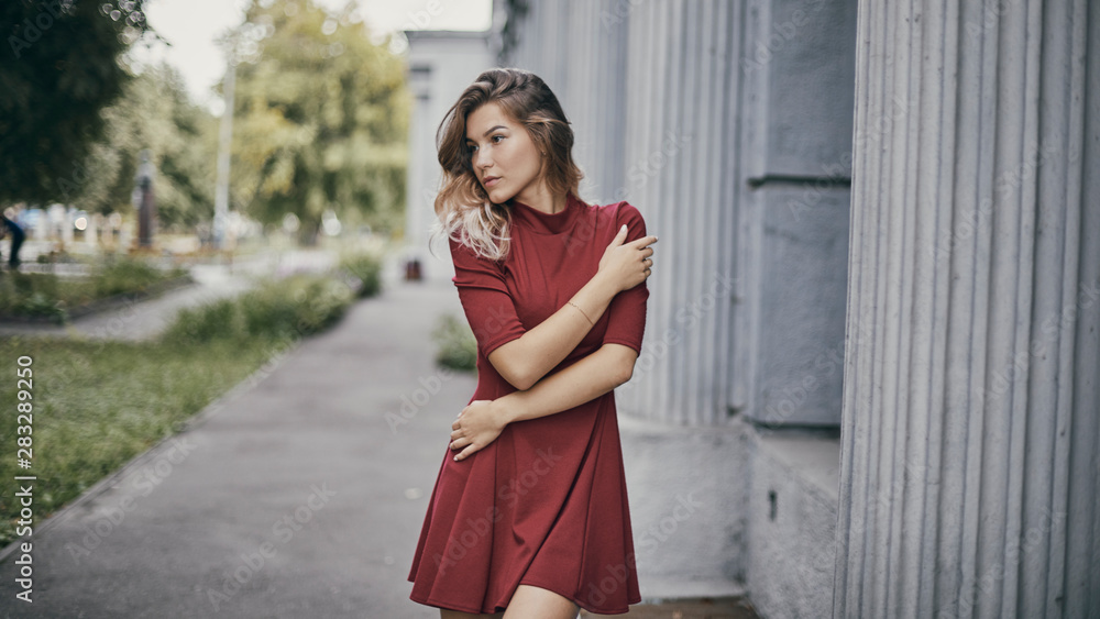 Nice tanned stylish brunette girl in red short dress with flowers is standing poses and flirting walking on the street city Nice tanned stylish brunette girl in red short dress with flowers is standing poses and flirting walking on the street city