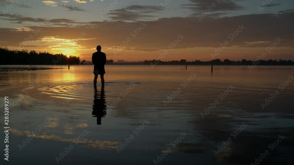 sunrise silhouette of a senior man standing in shallow water and practicing a palm tree yoga pose, Boyd Lake State Park in northern Colorado sunrise silhouette of a senior man standing in shallow water and practicing a palm tree yoga pose, Boyd Lake State Park in northern Colorado