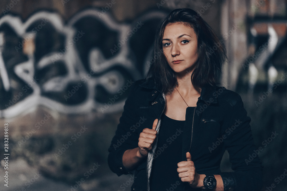Mysterious beautiful woman in black bodysuit and leather jacket with henna tattoo on her legs sitting on old stone steps with ornate carved balustrade while looking at the camera Mysterious beautiful woman in black bodysuit and leather jacket with henna tattoo on her legs sitting on old stone steps with ornate carved balustrade while looking at the camera