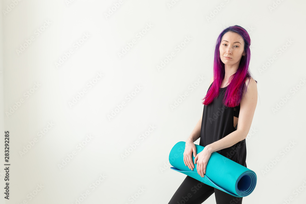 Young nice girl hipster with colored hair holding in hand a sports mat posing on a white background. Healthy lifestyle concept. Advertising space. Young nice girl hipster with colored hair holding in hand a sports mat posing on a white background. Healthy lifestyle concept. Advertising space.